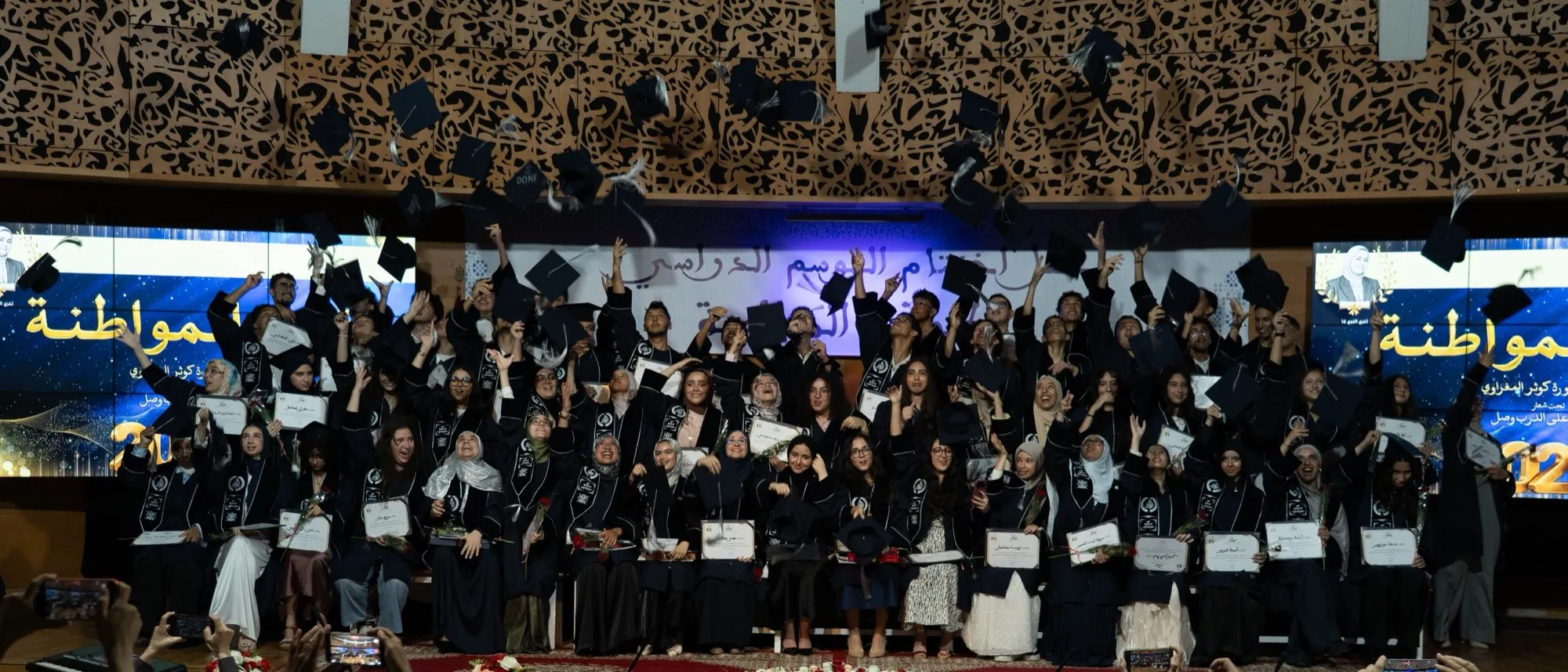 The graduating class tossing their mortarboard caps in the air in celebration, diplomas in hand